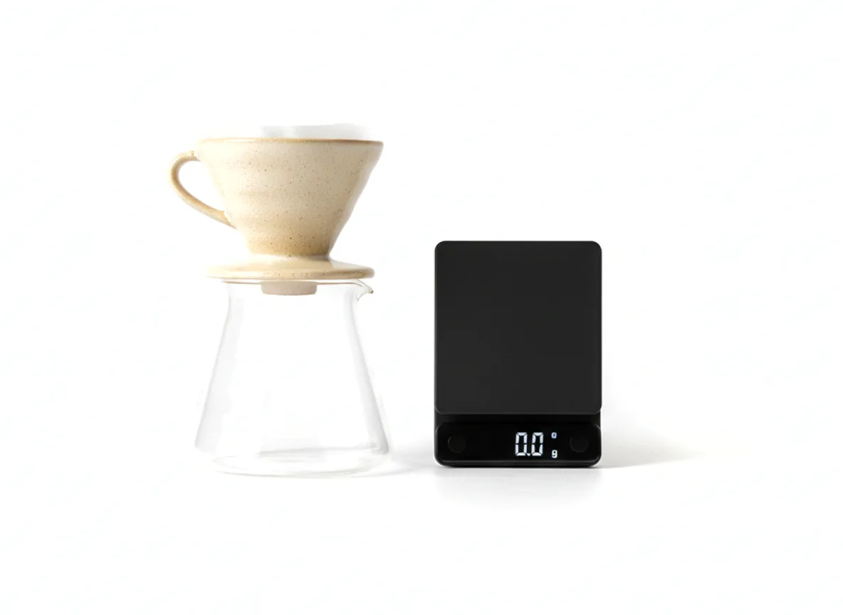 A pour-over cone, a glass carafe and a scale arranged on white.