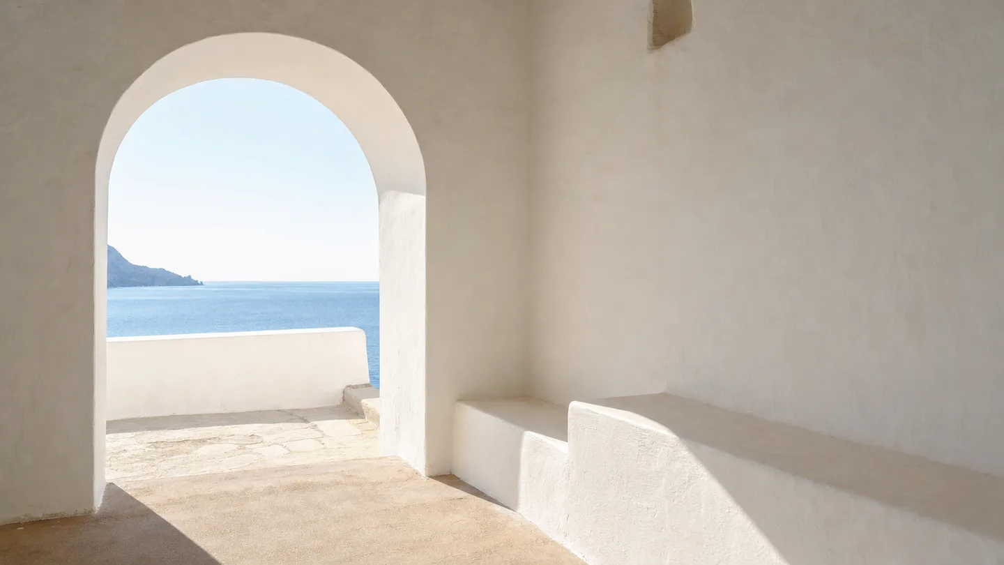 A sunlit whitewashed terrace with a deep arched opening framing a calm blue sea