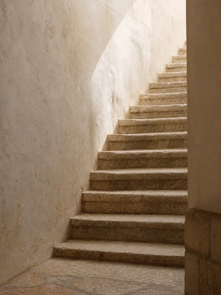 A sunlit stone stairwell climbing toward warm daylight from above