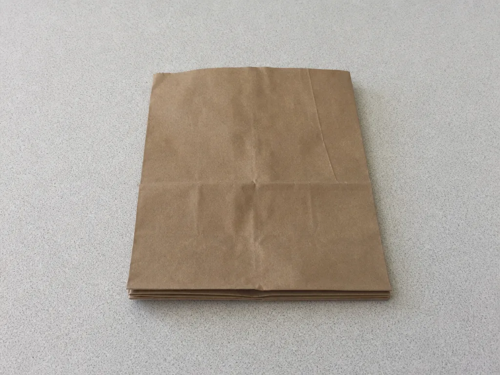 A folded blank paper bag resting flat on a plain formica table, its creases catching the light.