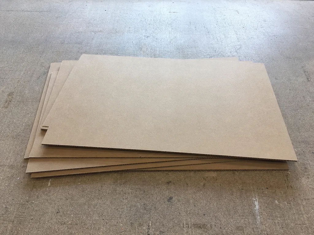 A stack of plain blank cardboard sheets lying slightly askew on a bare workbench.