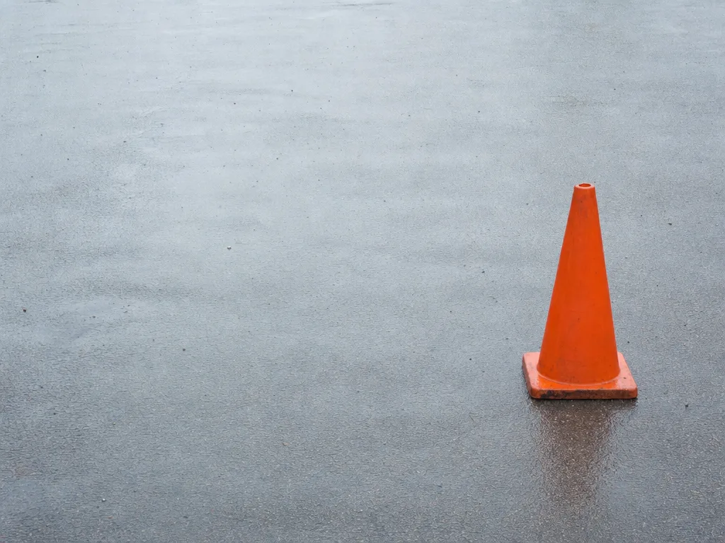 A single orange traffic cone standing off-centre to the right on wet grey tarmac.