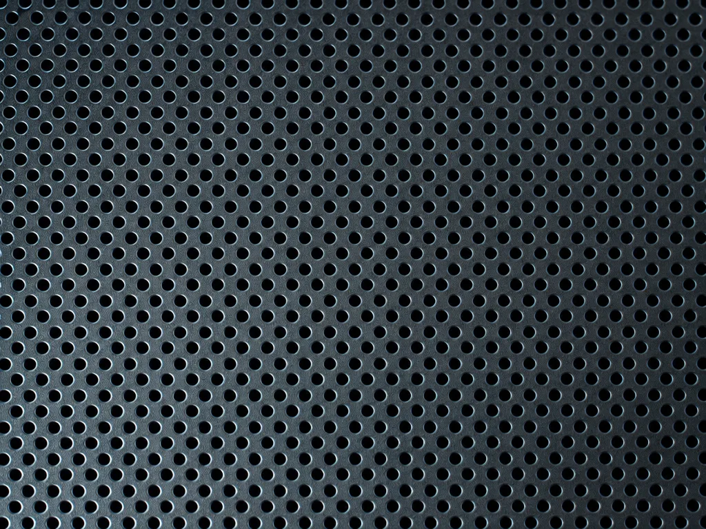 A fine perforated steel mesh filling the frame under hard cool raking light, sharp macro detail in cold near-black tones.