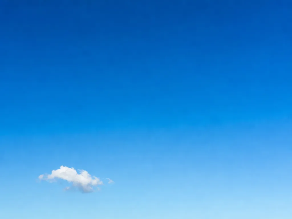 A calm high-key gradient of midday sky with a single small bright cloud low to one side.