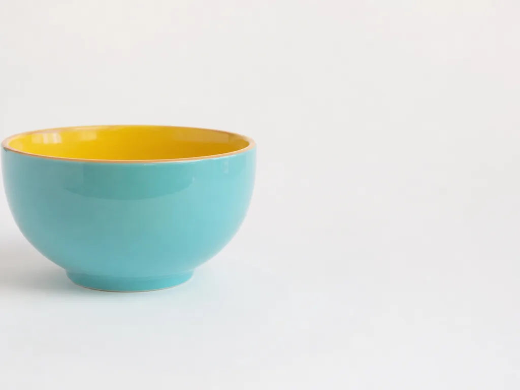 A smooth colorful ceramic bowl pushed to one side of a bright studio background.