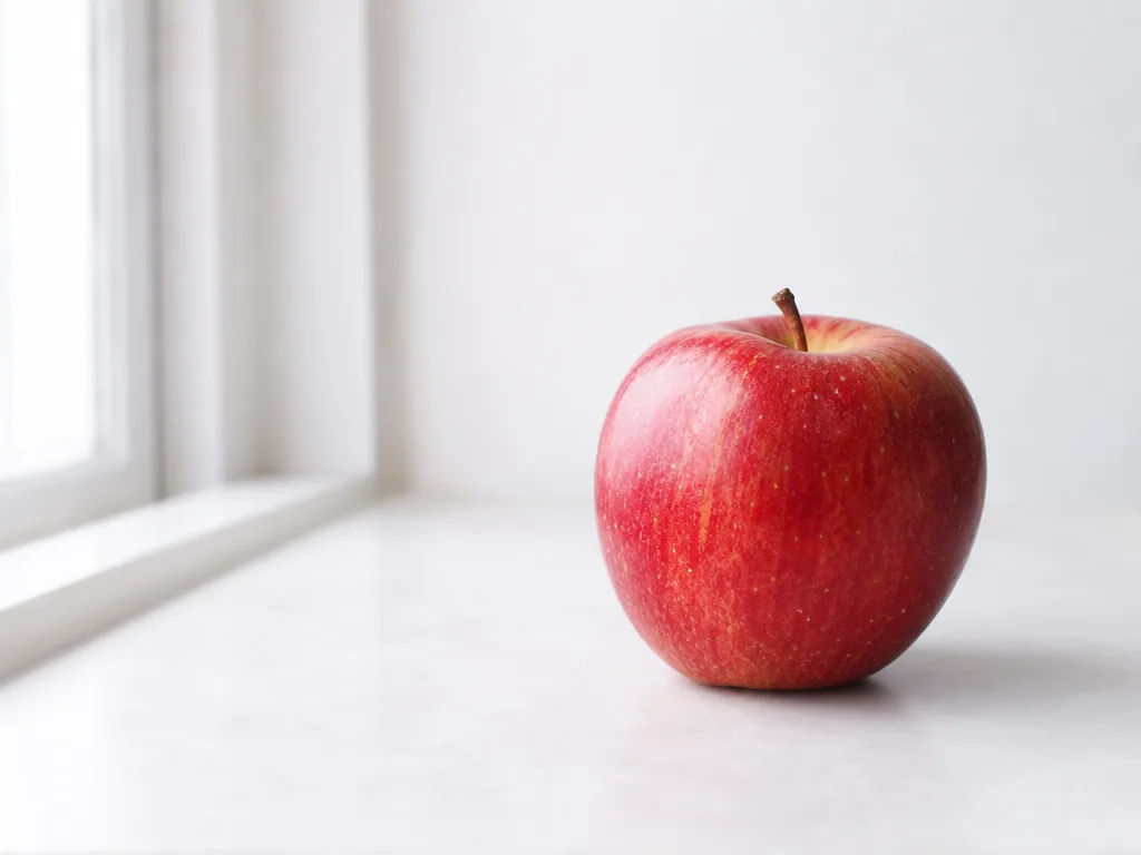 A single ripe apple on a plain pale tabletop, off-center — the untouched source image.