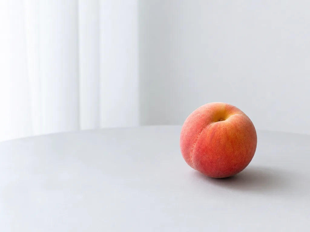 A single peach on a pale tabletop — the source image.